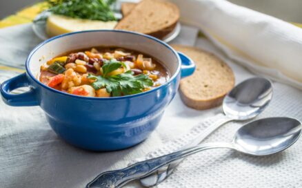 minestrone soup in a blue bowl with two spoons and sliced bread in the background