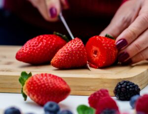 Female slicing strawberries with a kitchen knife in front of fresh strawberries